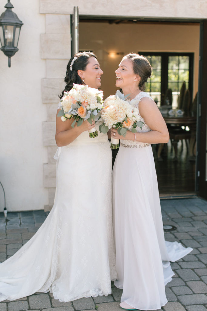 Two LGBTQ Brides laughing and holding matching peach and cream bouquets