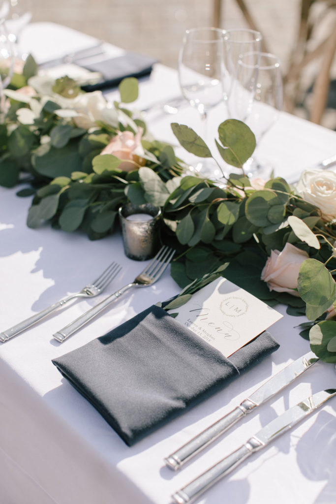 wedding table set with garland and peach flowers with a custom menu card wrapped in a napkin