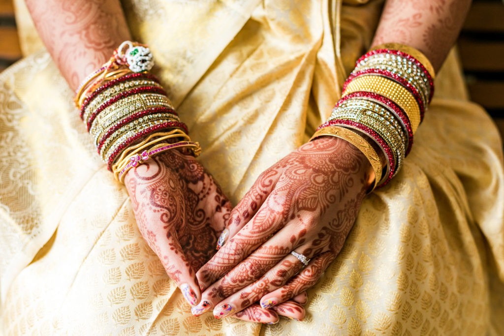 Wedding Henna or mendhi with glass bangles on brides hands with her engagement ring