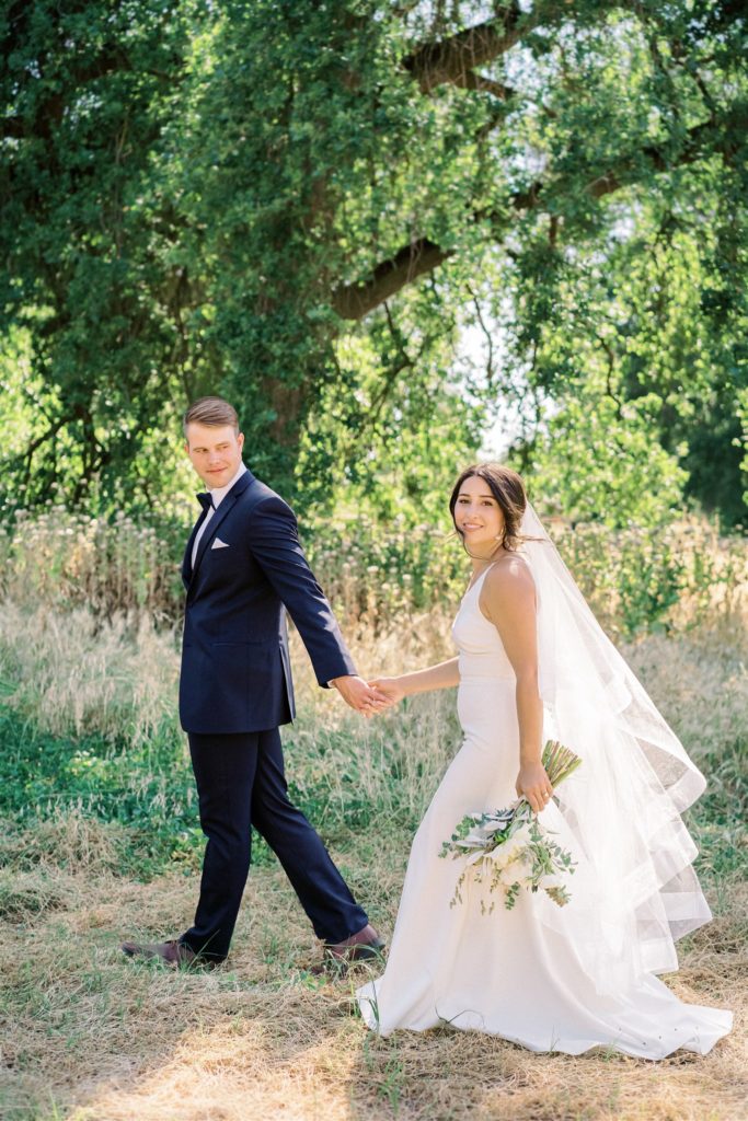 Bride and groom walking hand in hand in green setting