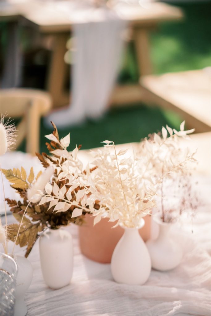 Small white pottery vases on table with dried grasses and bleached ferns. 