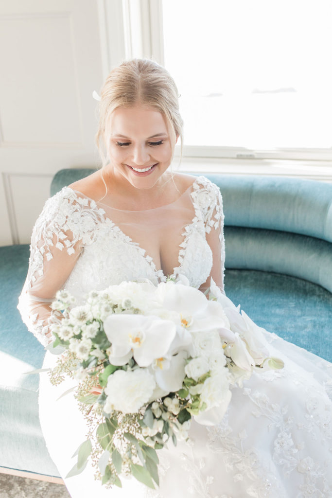 Bride on blue sofa with a classic orchid filled bouquet