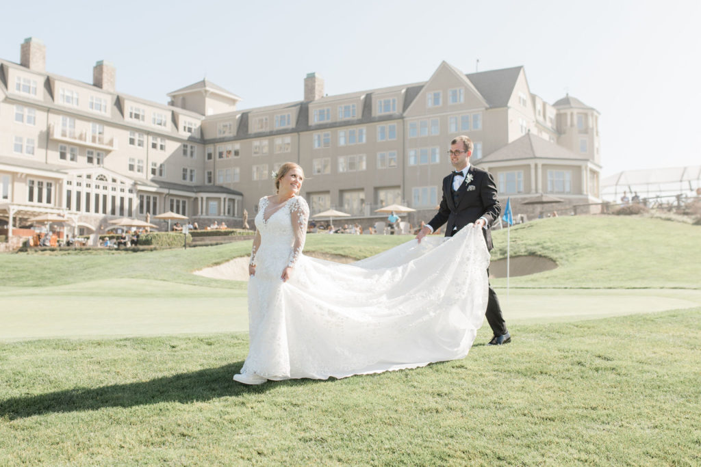 Groom holding Bride's dress train walking in front of Golf Resort